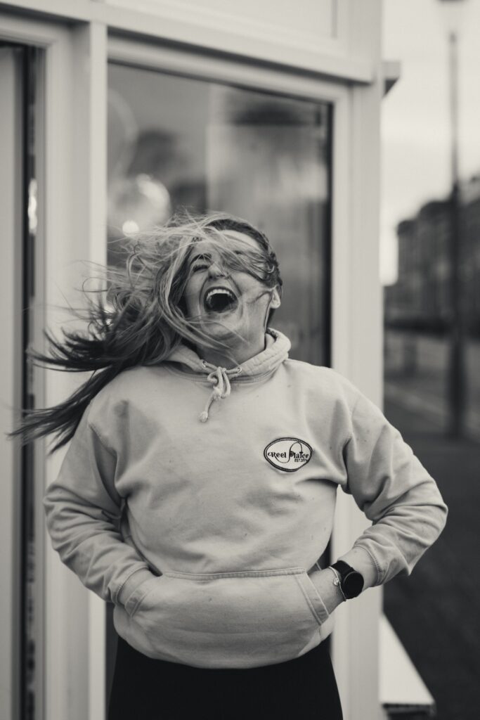 Candid branding shot of a woman laughing with wind in her hair outside her Ayrshire business.