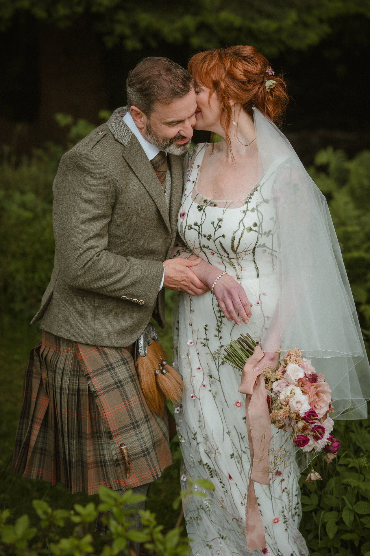 Bride whispering in the groom’s ear during their outdoor wedding in Ayr, captured candidly.