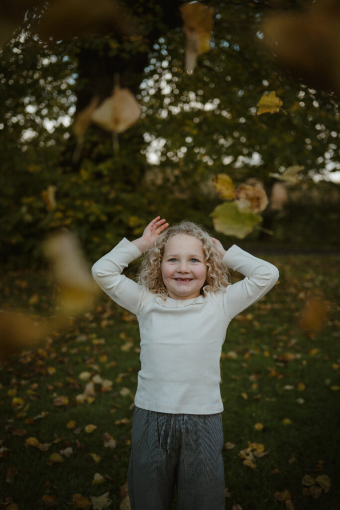 Ayrshire family photoshoot, child throwing autumn leaves during a natural outdoor session.