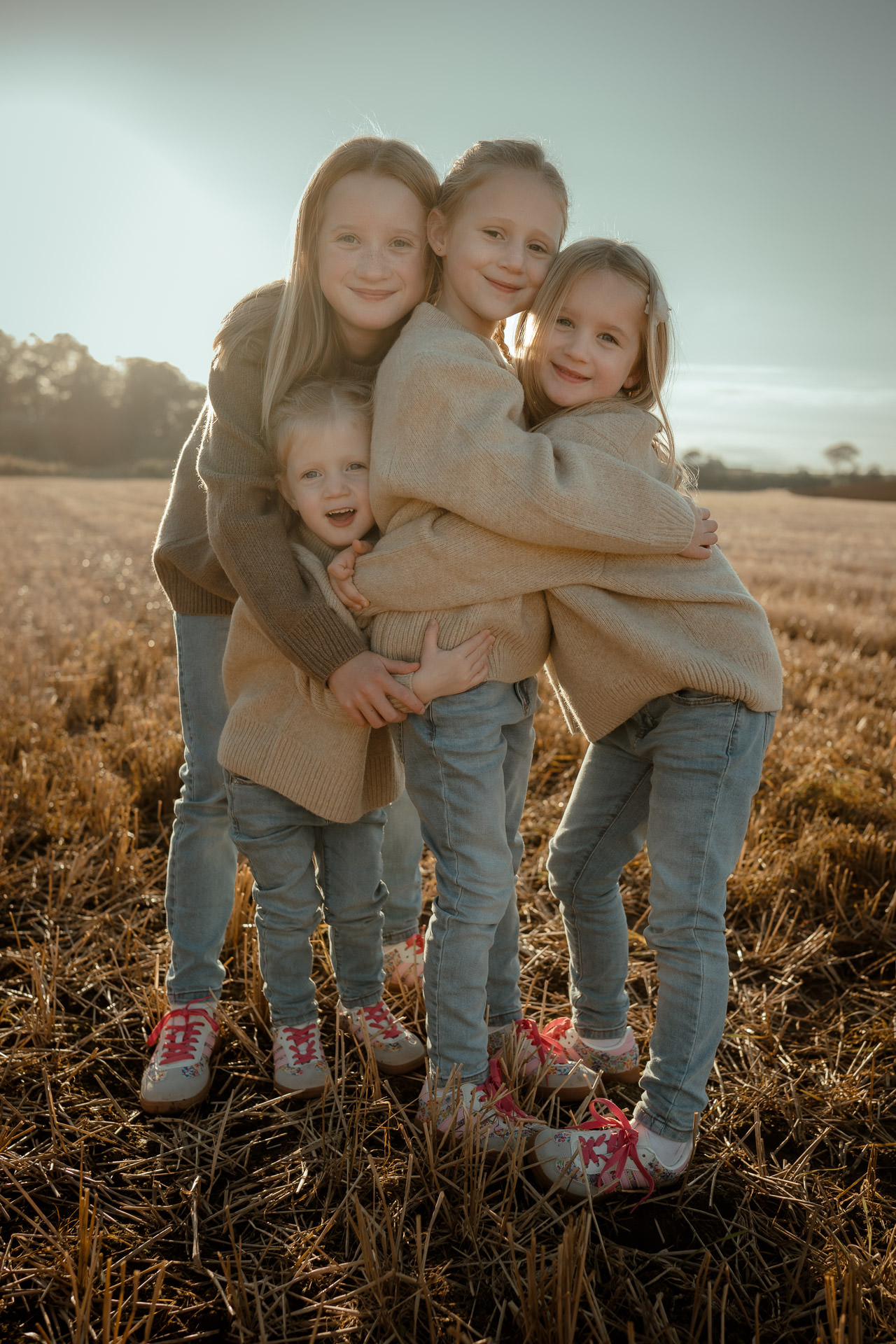 Children hugging each other in a golden field at sunset in Ayrshire.