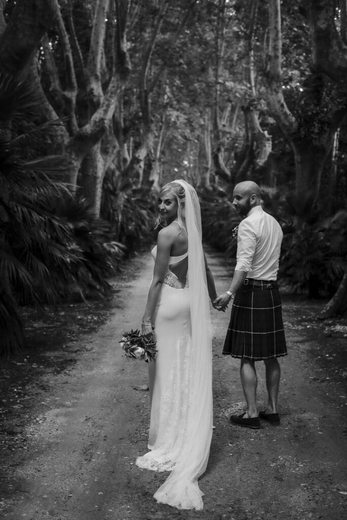 Bride and groom walking hand in hand down a tree-lined path on their wedding day.