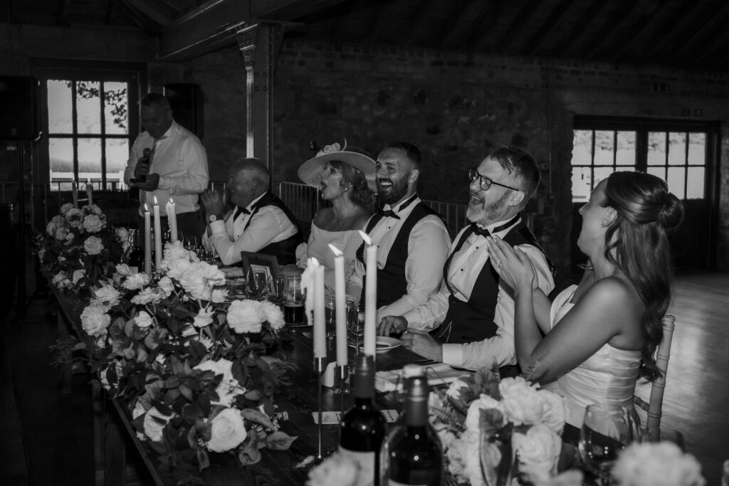 Bride and groom laughing with family during wedding speeches at their reception.