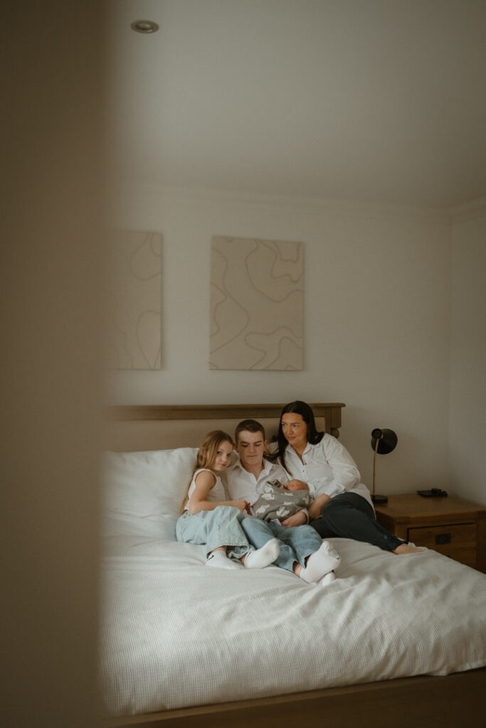 A mother sitting on the bed with her newborn baby and older children.