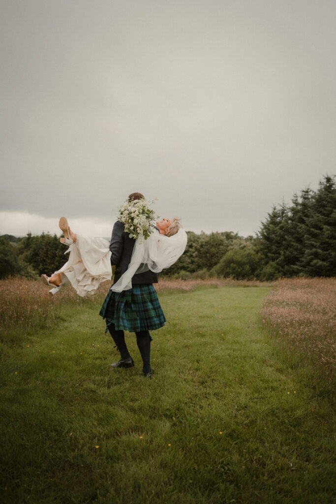 Groom carrying his bride through a meadow after their Ayrshire wedding ceremony