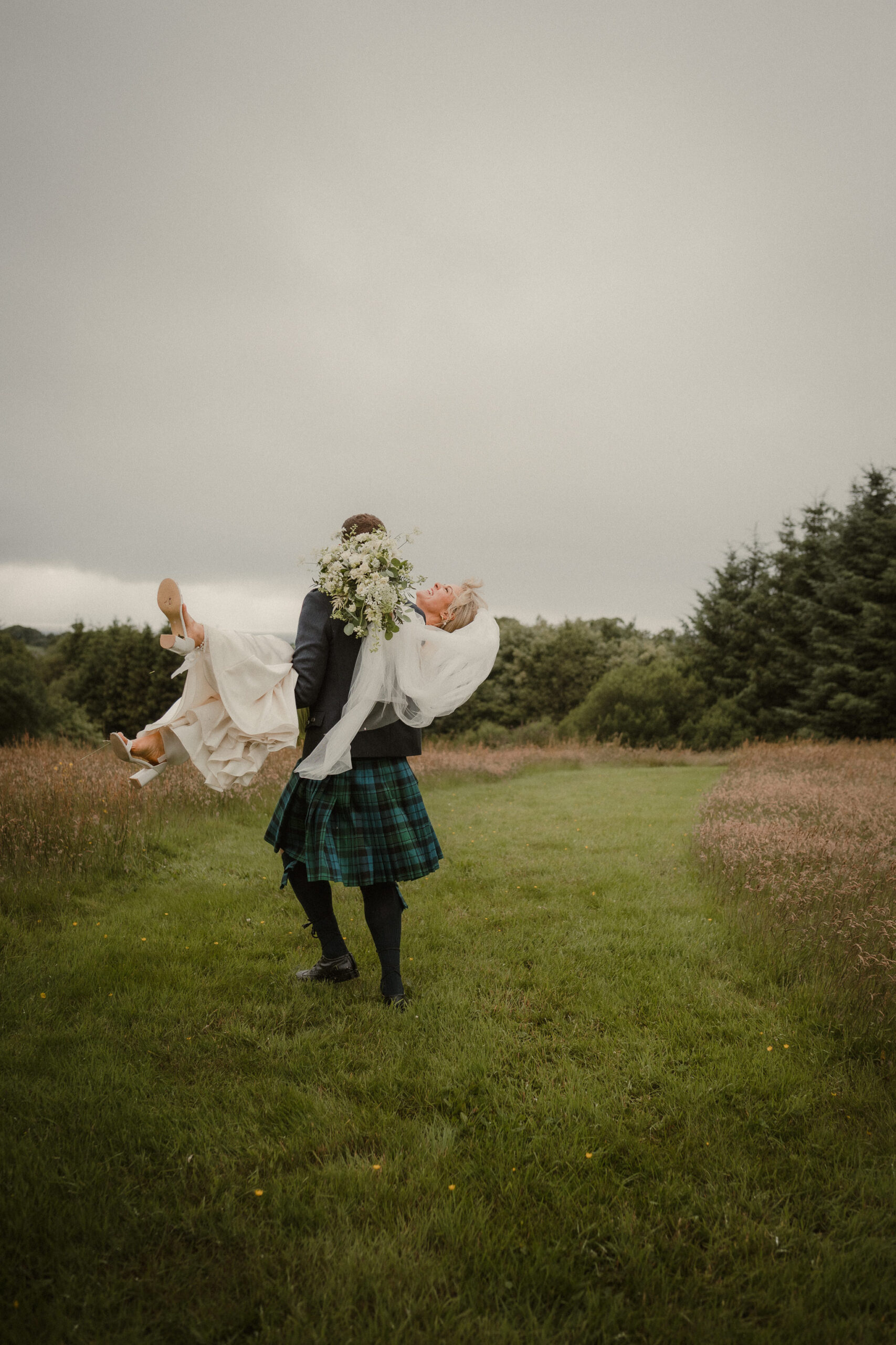 Groom carrying his bride through a meadow after their Ayrshire wedding ceremony