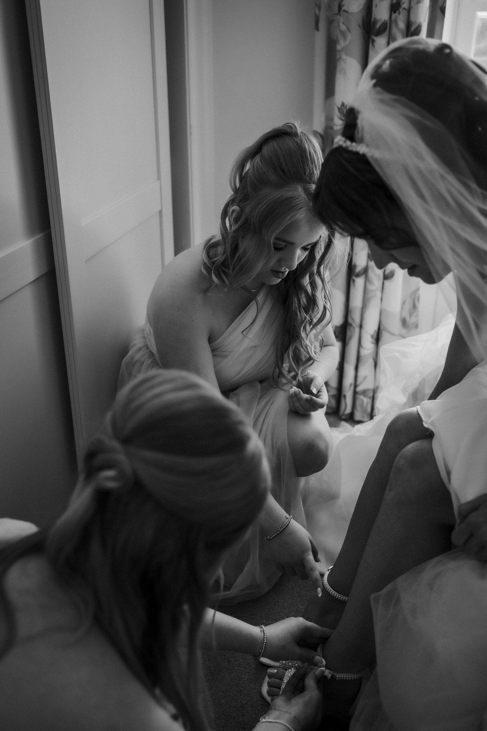 Bridesmaids helping with the bride's shoes before during preparations.
