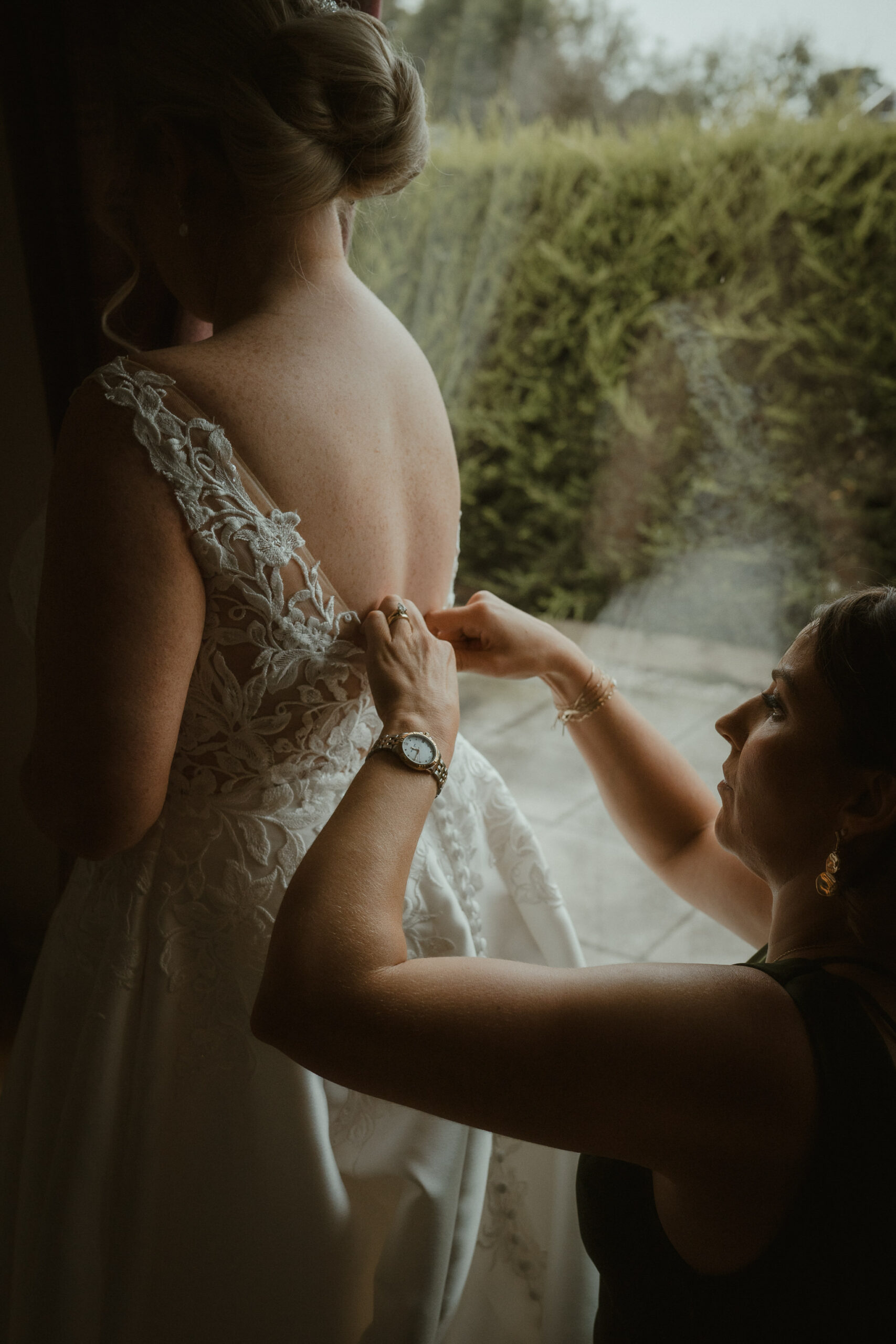 Bride’s dress being fastened by the window as she gets ready at home in Fenwick
