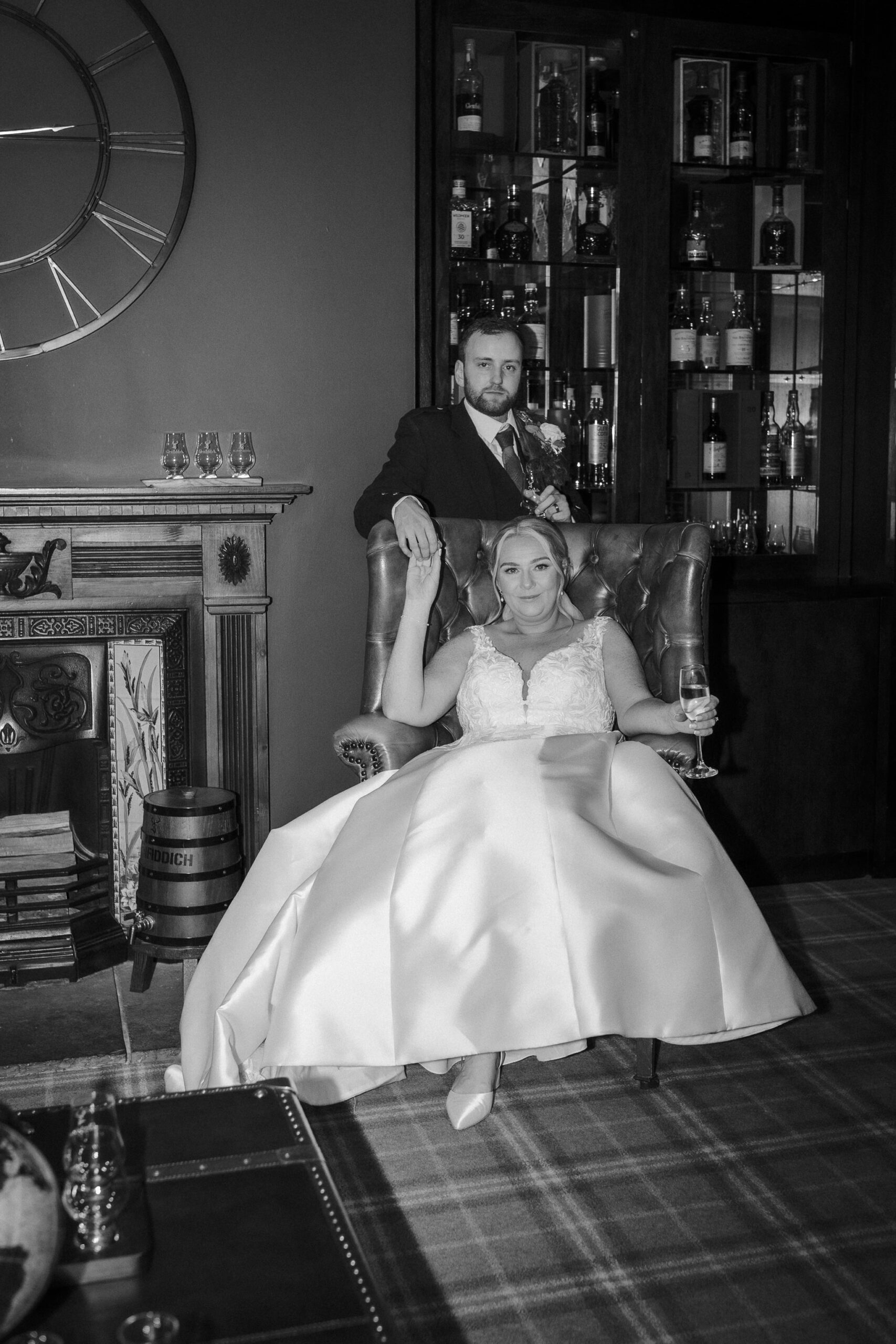 Bride in a leather armchair with the groom beside her in the Whisky Library at Enterkine House