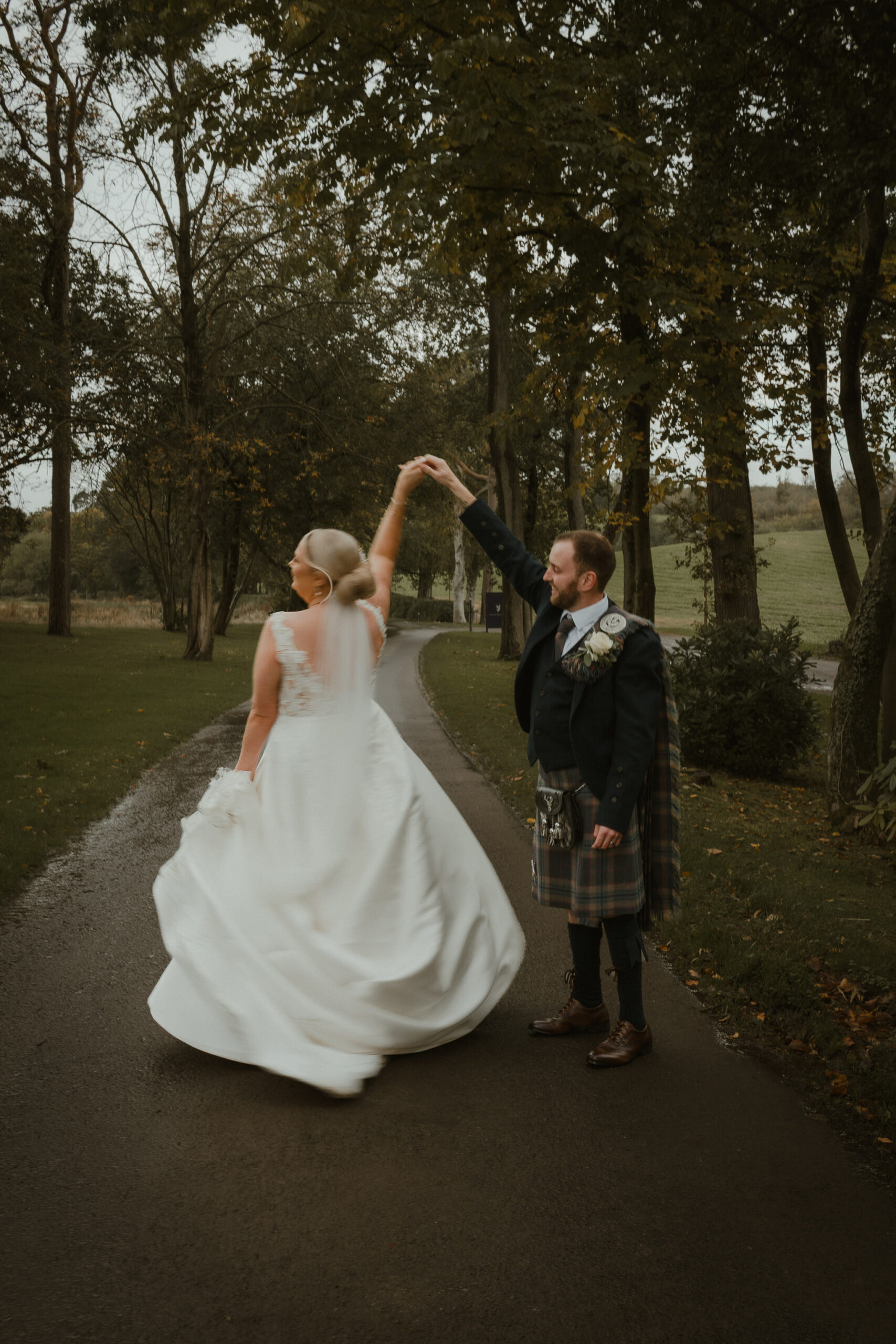 Groom twirling the bride under the trees on the drive at Enterkine House, Ayrshire